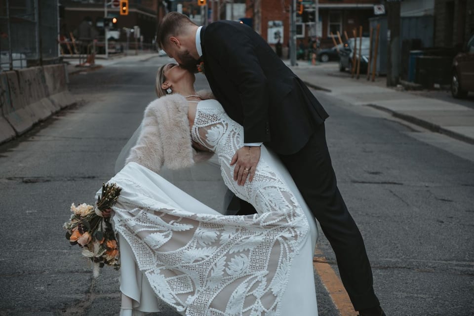 A bride and groom share a dip kiss in the middle of a Hamilton street, her lace gown and dried-flower bouquet trailing.