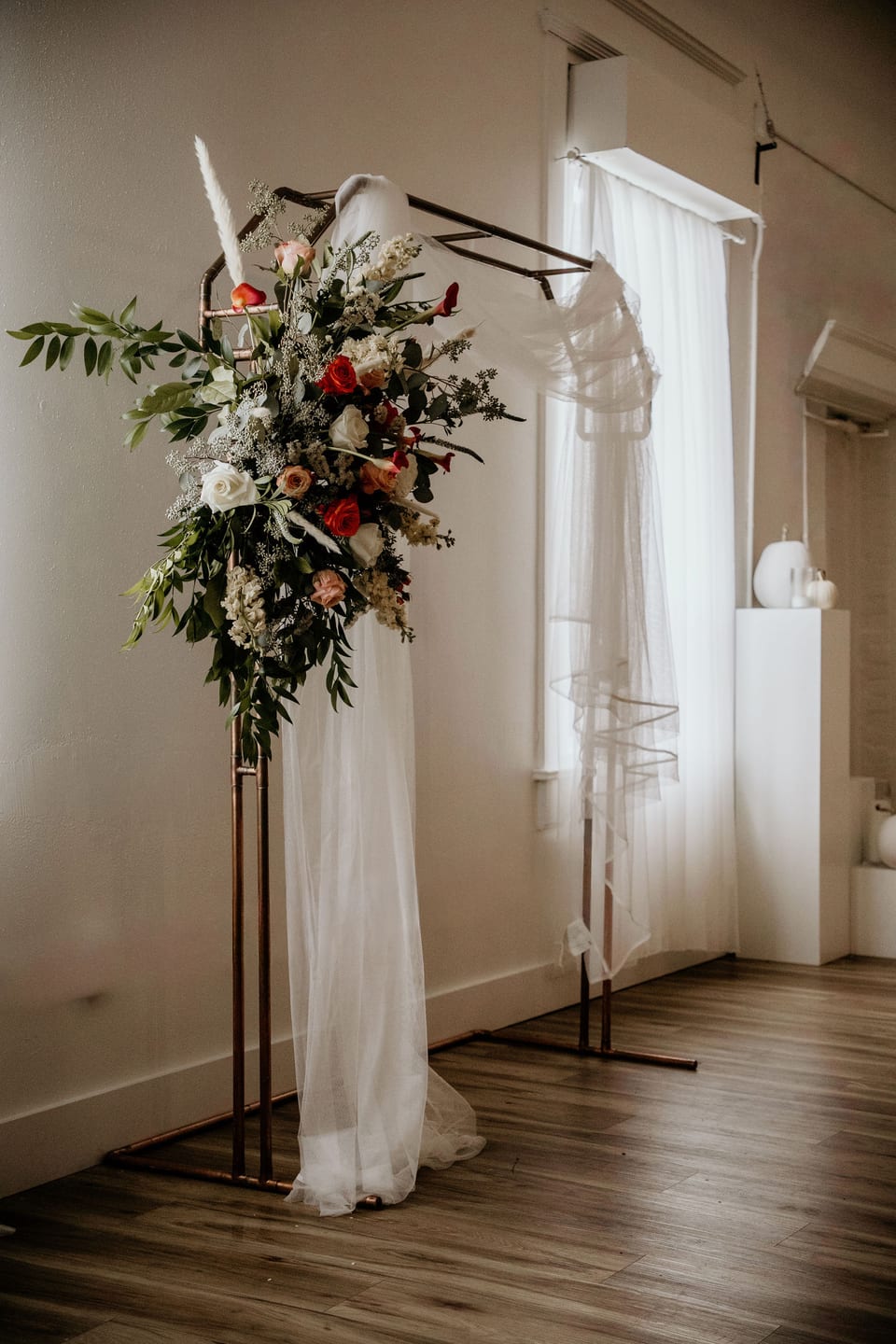 Tall floral arrangement beside a sunlit window at the ceremony.
