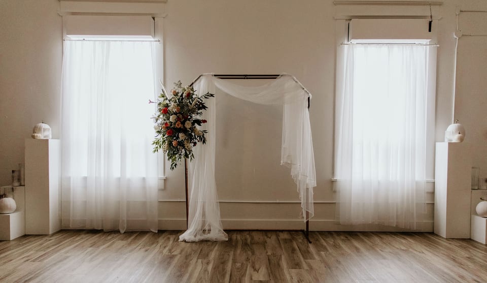 Minimal ceremony space with a floral pillar and tall windows.