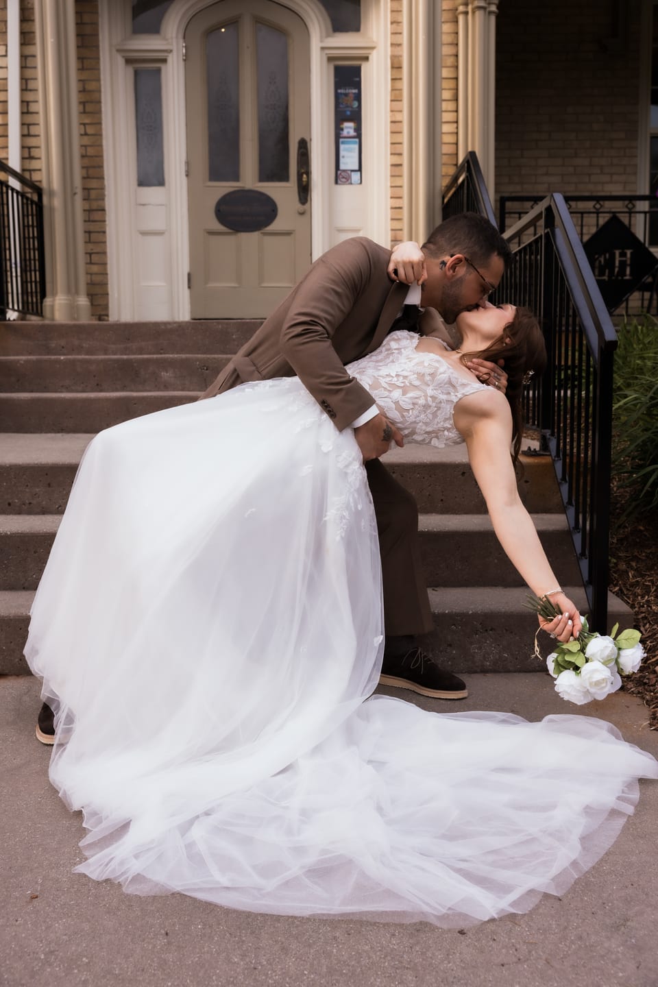 A dramatic dip kiss on the front steps of a historic building, her tulle train pooling on the stairs.