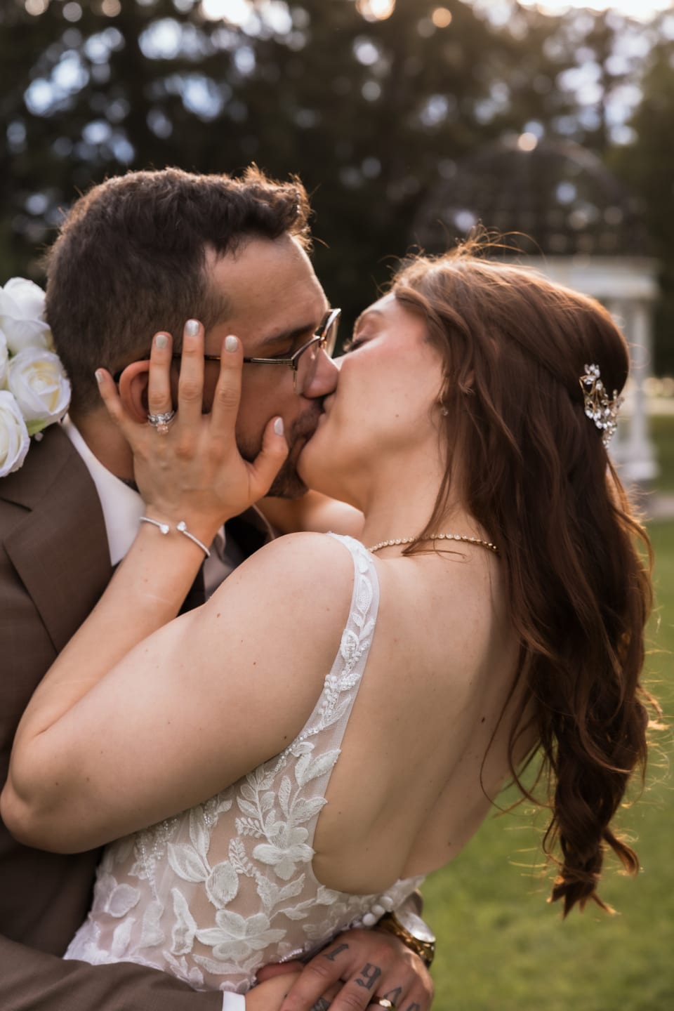 The couple share a kiss in golden-hour light, her hair catching the breeze with the sunset glowing behind them.