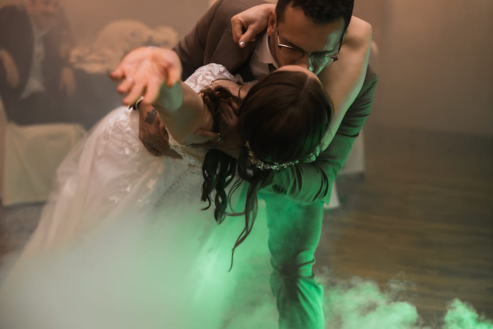 A dramatic reception dip kiss lit in green uplighting with fog rolling across the dance floor.