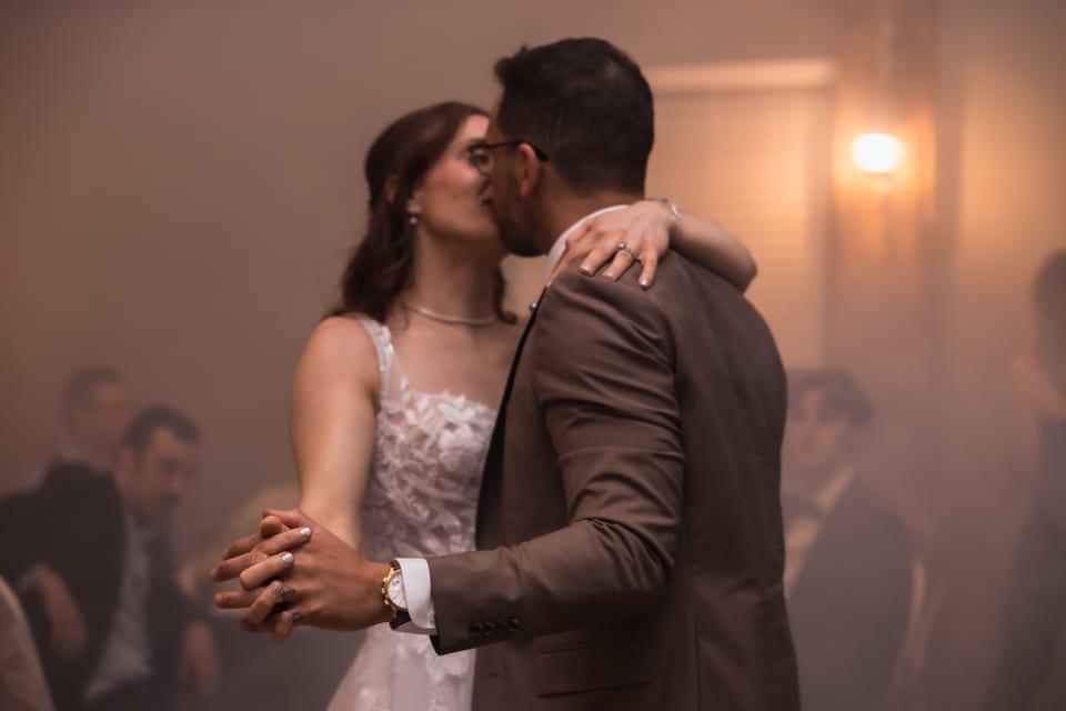 Bride and groom slow dance close together, softly lit through haze at the reception.