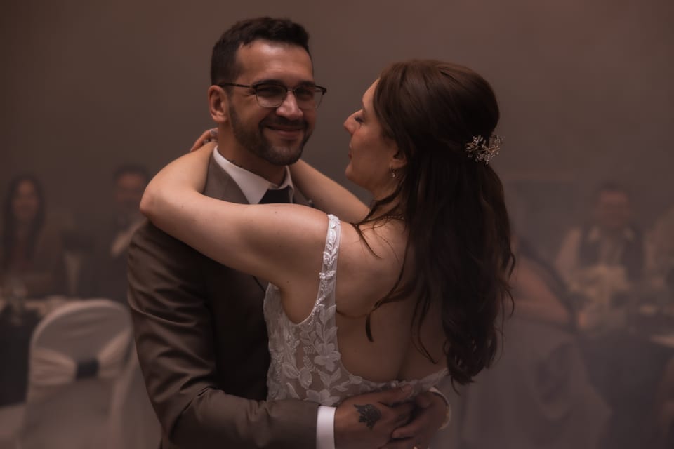 The bride rests her head close as they slow dance, her hairpiece catching the warm reception light.